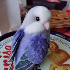 May include: A plush purple and white bird toy with a black eye. The bird is sitting on a tin with a red and white design.