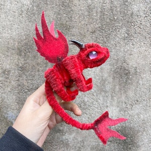 May include: A red felt dragon with a long tail and wings. The dragon has a black horn and purple eyes.