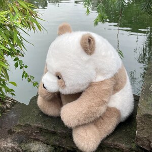 Peut inclure: Une peluche panda avec une fourrure douce couleur crème sur la tête et le dos, contrastée par une fourrure brun clair sur les oreilles, le contour des yeux, les bras et les jambes. L'animal en peluche a un petit nez noir et des yeux sombres.
