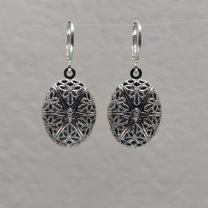May include: A pair of silver oval earrings with a delicate filigree design. The earrings have a starburst pattern in the center and are suspended from a simple hoop.