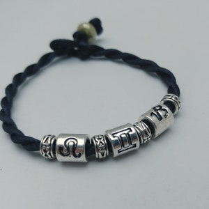 May include: A black braided cord bracelet with silver beads. The beads have zodiac symbols and the number 13.