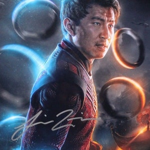 以下が含まれることがあります： マーベル・スタジオ映画「シャン・チー／テン・リングスの伝説」の映画ポスター。ポスターには、赤と黒の衣装を着た武術家、シャン・チーが、青とオレンジの背景の前に立っている様子がクローズアップされている。ポスターには、映画のタイトルと公開日も記載されている。