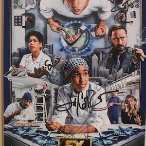 May include: Poster depicting a kitchen scene with several people, mainly chefs, in action. The image includes the text "FX THE BEAR" at the bottom, with signatures across the image. The colour scheme is primarily blue, white, and various skin tones.