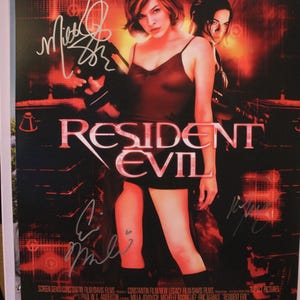Könnte beinhalten: Ein Filmplakat für "Resident Evil" mit Milla Jovovich und Michelle Rodriguez. Das Plakat hat ein rotes und schwarzes Farbschema mit dem Titel in großen, fetten Buchstaben. Die Unterschriften der Schauspieler sind sichtbar.