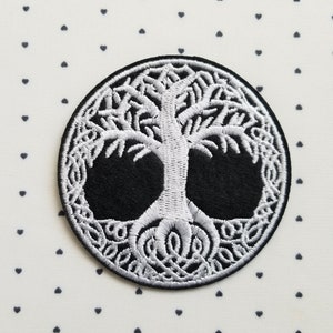 May include: A circular embroidered patch featuring a white Celtic tree of life design on a black background. The tree's branches and roots are intricately detailed. The patch is surrounded by a black border.