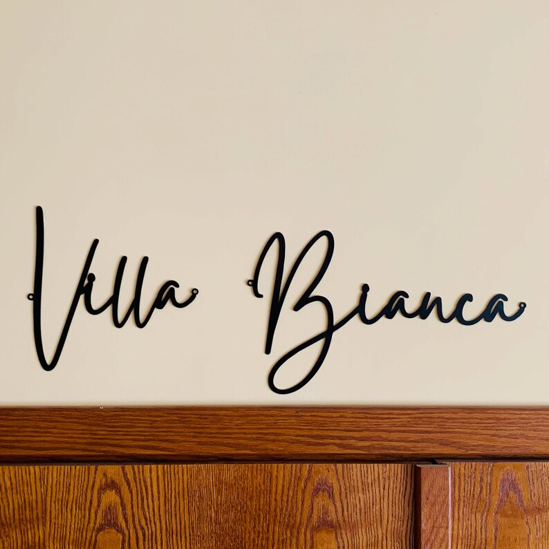 May include: Black metal wall decor with the words "Villa Bianca" in a cursive script font.