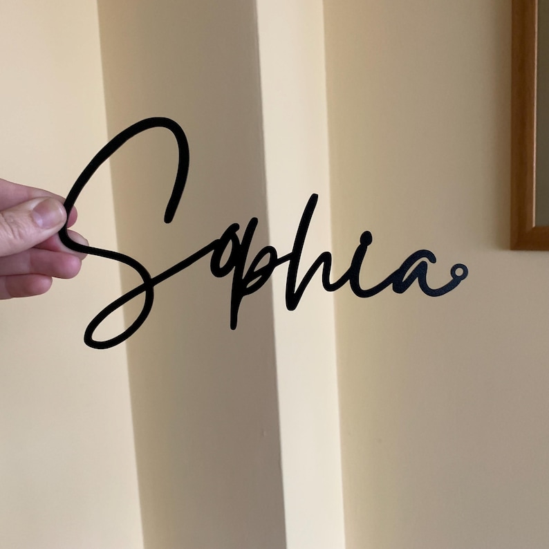 May include: Black metal cutout of the name "Sophia" in a cursive script font.