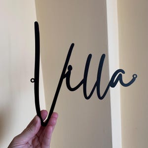 May include: Black metal wall decor with the word "Villa" written in a cursive script.