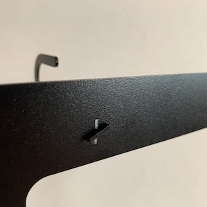 Pu&ograve; includere: Mensola a muro in metallo nero con un gancio nella parte superiore e una piccola linguetta in metallo sul lato.
