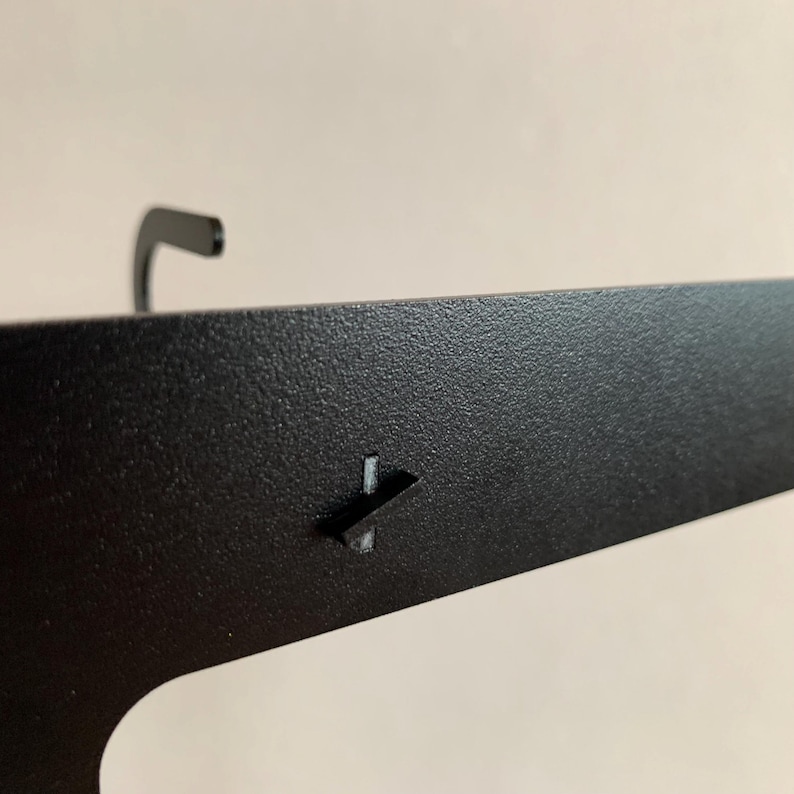 Pu&ograve; includere: Mensola a muro in metallo nero con un gancio nella parte superiore e una piccola linguetta in metallo sul lato.