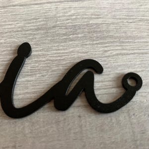 May include: Black metal cutout of the letter "w" in a cursive style. The letter has a hole at the end of the right curve.