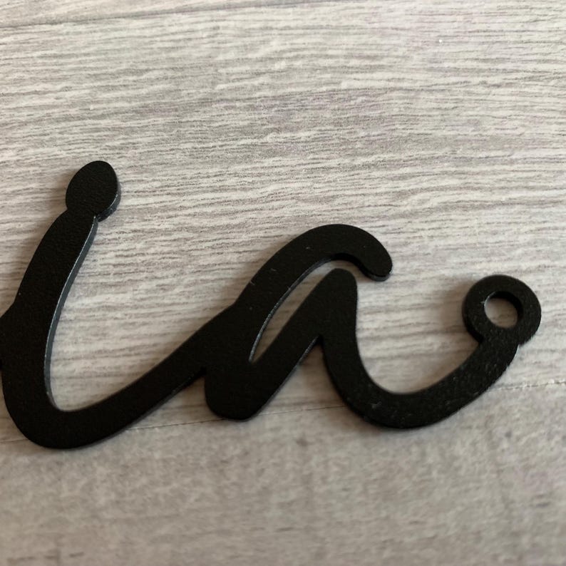 May include: Black metal cutout of the letter "w" in a cursive style. The letter has a hole at the end of the right curve.