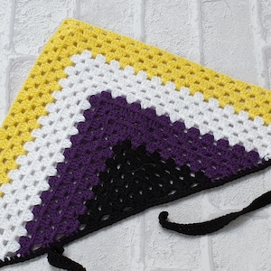 May include: A crocheted triangular scarf in yellow, white, purple and black. The scarf has a black tie string.