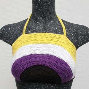 Può includere: Un top halter lavorato a uncinetto con uno schema di colori giallo, bianco, viola e nero. Il top ha la forma di un semicerchio, con i colori disposti a strisce.