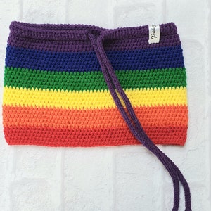Puede incluir: Una bolsa de cordón de crochet arcoíris con una etiqueta morada que dice "Pride".