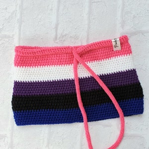 Puede incluir: Una bolsa de crochet con un patrón de rayas rosa, blanco, morado, negro y azul. La bolsa tiene un cierre de cordón y una pequeña etiqueta que dice "Pride".