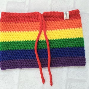 Puede incluir: Un top de crochet arcoíris con un cordón de ajuste rojo. El top tiene una etiqueta que dice "Pride".