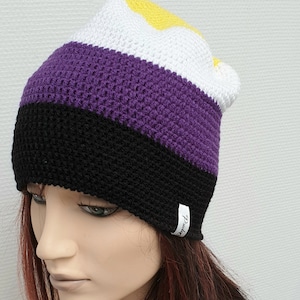 Könnte beinhalten: Eine gestrickte Mütze in Lila, Schwarz, Weiß und Gelb mit einem weißen Etikett, auf dem "Pride" steht.