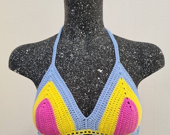 Puede incluir: Un top de bikini de ganchillo con un esquema de color azul, amarillo y rosa. El top tiene forma de triángulo y un borde festoneado.