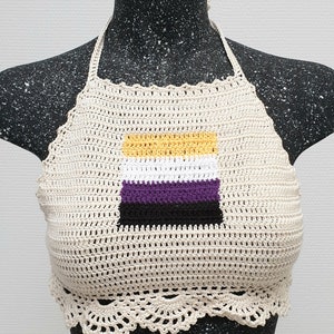 Op de afbeelding: Crèmekleurige, gehaakte haltertop met de non-binaire pride-vlag. De vlag is een rechthoek met horizontale strepen in geel, wit, paars en zwart. De top heeft een geschulpte rand en wordt getoond op een mannequin.