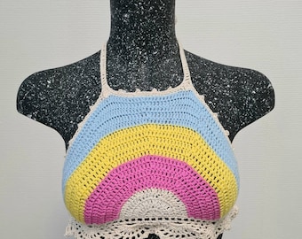 Puede incluir: Un top halter de crochet arcoíris con un esquema de colores azul claro, amarillo, rosa y beige. El top tiene un ribete de crochet alrededor del escote y el borde inferior.