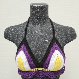 Op de afbeelding: Een gehaakt bikini-top met een paarse, witte en gele kleurstelling. De top is gemaakt met een delicate haaksteek en heeft een gegolfde rand.