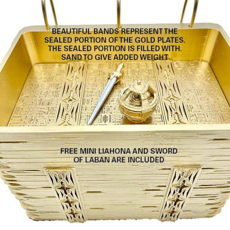 May include: A gold-coloured, rectangular box with a decorative design. The box is filled with sand and contains a small sword and a round object. The text on the box reads: "BEAUTIFUL BANDS REPRESENT THE SEALED PORTION OF THE GOLD PLATES. THE SEALED PORTION IS FILLED WITH. SAND TO GIVE ADDED WEIGHT FREE MINI LIAHONA AND SWORD OF LABAN ARE INCLUDED"
