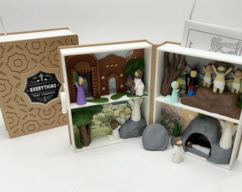 May include: A wooden box shaped like a book with a diorama inside depicting the story of Easter. The box is open and shows a scene of Jesus entering Jerusalem, a scene of Jesus in the tomb, and a scene of Jesus rising from the tomb. The box is decorated with a brown and white pattern and the text "The Need Everything That Changed".