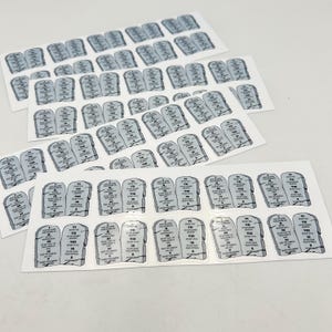 May include: A sheet of stickers featuring the Ten Commandments written on stone tablets. Each sticker has a Roman numeral indicating the commandment number.