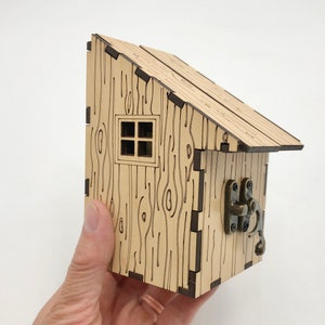 May include: A small wooden house with a brown roof and a window. The house has a wood grain pattern and a metal latch on the side.