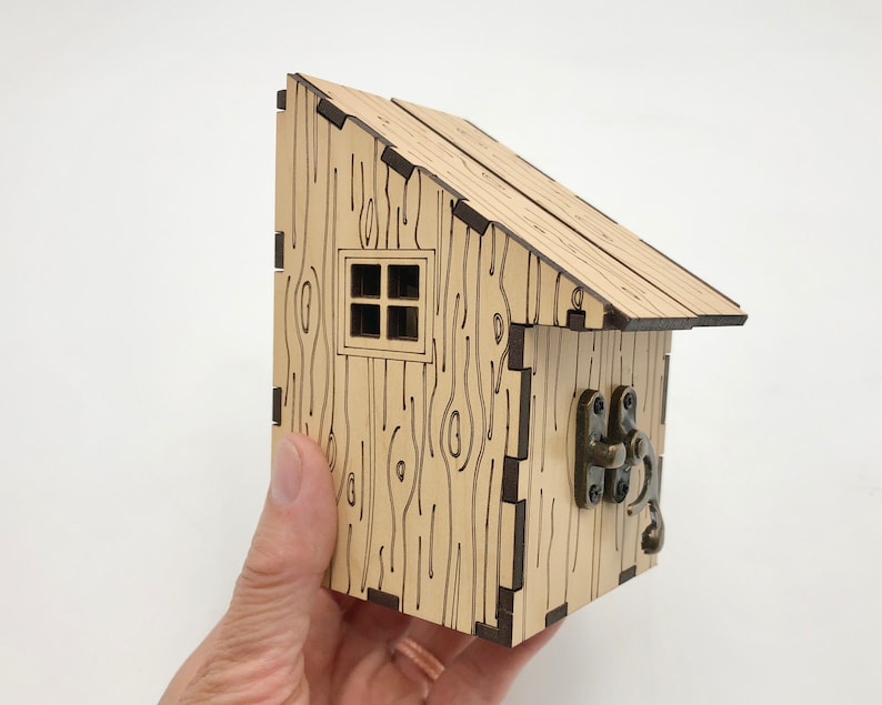 May include: A small wooden house with a brown roof and a window. The house has a wood grain pattern and a metal latch on the side.
