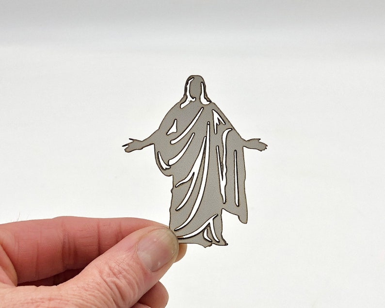 May include: A laser cut wooden silhouette of a person in a robe with their arms outstretched.