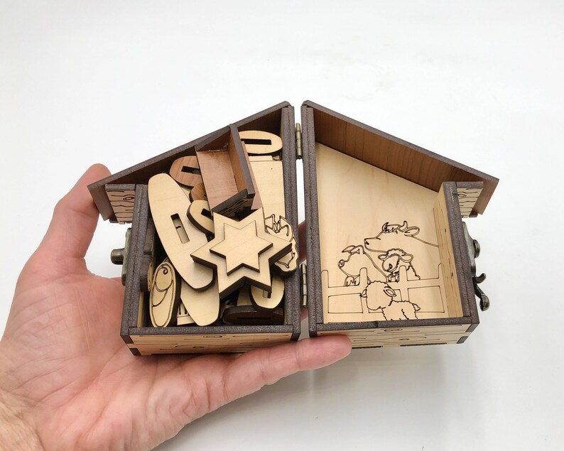 May include: A wooden box with a hinged lid, open to reveal a nativity scene with a star, animals, and a manger. The box is made of light brown wood and has a dark brown stain.