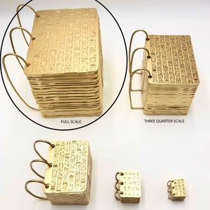 May include: Five gold-coloured metal books with a decorative pattern on the cover. The books are arranged in a row from largest to smallest. The books are labelled "Full Scale", "Three Quarter Scale", "Half Scale", "One Quarter Scale", and "Mini Doll Size".