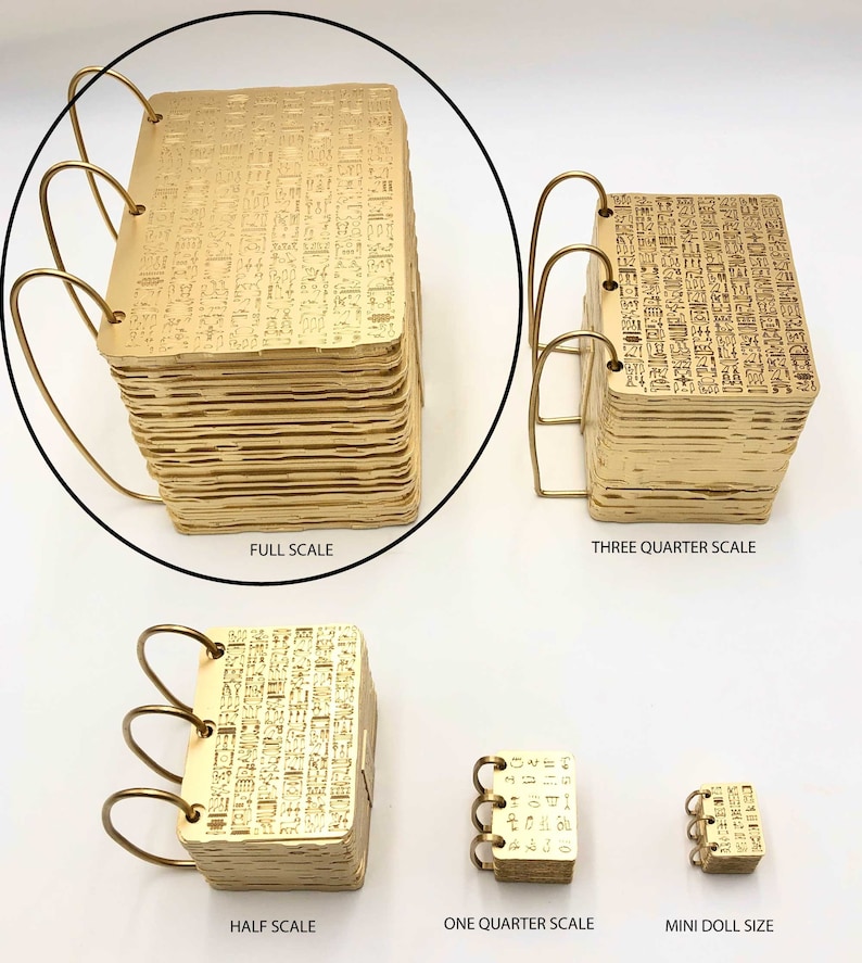 May include: Five gold-coloured metal books with a decorative pattern on the cover. The books are arranged in a row from largest to smallest. The books are labelled "Full Scale", "Three Quarter Scale", "Half Scale", "One Quarter Scale", and "Mini Doll Size".