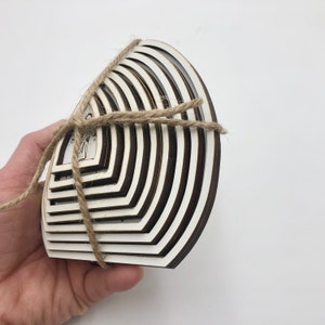 May include: A set of 10 white wooden circles with black edges, stacked in a graduated size, tied together with twine. The circles are arranged in a semi-circle shape.