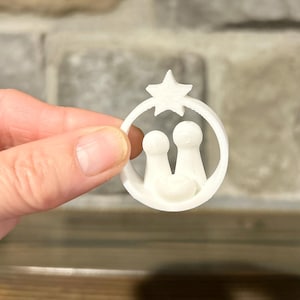 May include: White plastic ornament depicting the nativity scene with a star on top. The figures are of Mary, Joseph, and baby Jesus.
