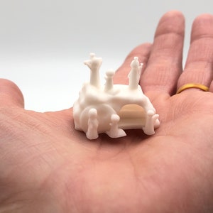 May include: White 3D printed model of a small castle with figures standing on top. The castle has a pointed roof and a small archway. The figures are all wearing simple robes.