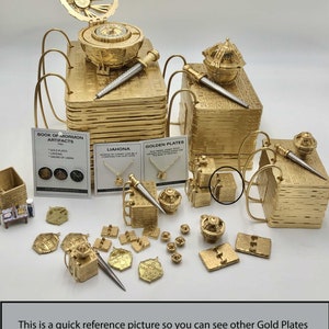 May include: A collection of gold-colored artifacts, including miniature books, pens, compasses, and jewelry. The image includes text that reads "BOOK OF MORMON ARTIFACTS" and "GOLDEN PLATES". The text also states "This is a quick reference picture so you can see other Gold Plates and Liahona items in my shop."