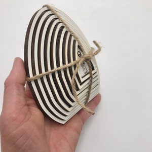 May include: A set of white wooden circles with a layered design, tied together with twine. The circles are arranged in a fan shape, with the largest circle at the bottom and the smallest circle at the top. The circles are decorated with a black and white design.