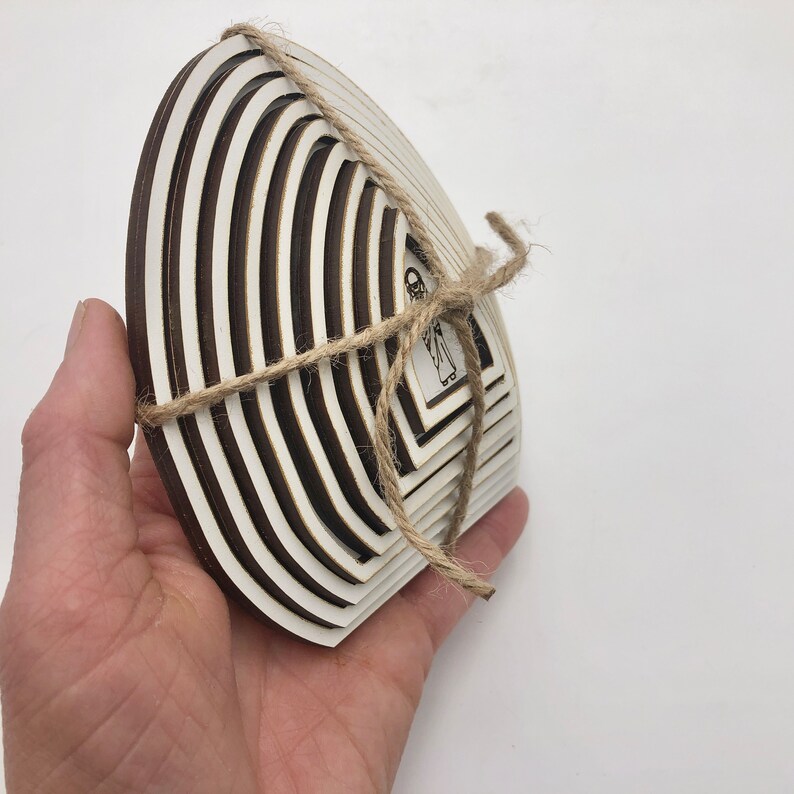 May include: A set of white wooden circles with a layered design, tied together with twine. The circles are arranged in a fan shape, with the largest circle at the bottom and the smallest circle at the top. The circles are decorated with a black and white design.