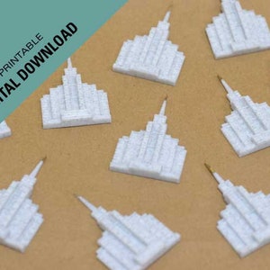 May include: Ten white 3D printed models of a temple, each with a spire on top. The models are arranged in a scattered pattern on a brown surface.