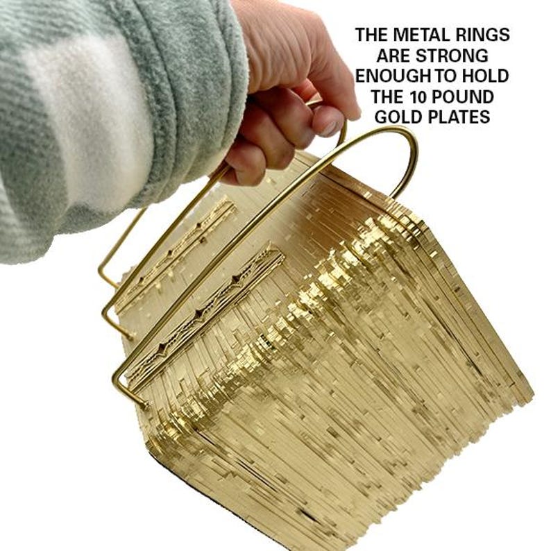 May include: A stack of gold-coloured metal plates held together by two brass rings. The rings are strong enough to hold 10 pounds of plates. The text "THE METAL RINGS ARE STRONG ENOUGH TO HOLD THE 10 POUND GOLD PLATES" is visible in the image.