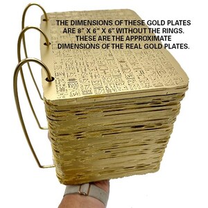 May include: A stack of gold-coloured plates with intricate designs, held by a hand. The plates are approximately 8 inches by 6 inches by 6 inches, excluding the rings. "THE DIMENSIONS OF THESE GOLD PLATES ARE 8" X 6" X 6" WITHOUT THE RINGS. THESE ARE THE APPROXIMATE DIMENSIONS OF THE REAL GOLD PLATES."