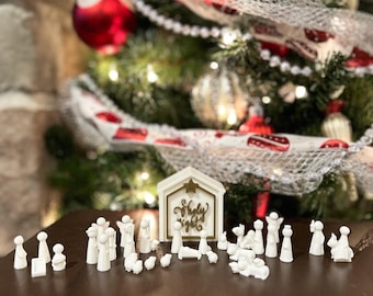 May include: White nativity scene set with a wooden stable that says "Holy Night" in gold lettering. The set includes figures of Mary, Joseph, baby Jesus, angels, shepherds, and animals.