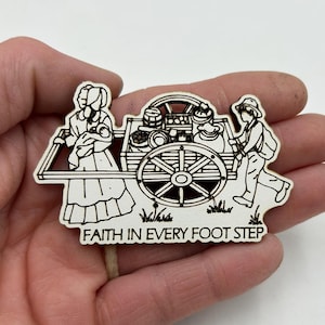 May include: Black and white wood cutout of a woman and a man pulling a cart filled with goods. The cart has a large wheel and the text "FAITH IN EVERY FOOT STEP" is below the image.