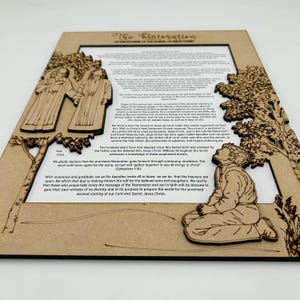 May include: A wooden framed print with a brown background and a light brown image of two figures in robes standing together. The text "The Restoration" is at the top of the frame. The text "God have mercy" is at the bottom of the frame. The text "We gladly declare that the promised Restoration goes forward through continuing revelation. The earth will never again be the same, as God will "gather together in one all things in Christ" (Ephesians 1:30)." is in the center of the frame.