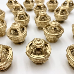 May include: A collection of gold-coloured, intricately detailed, spherical ornaments with a decorative design. The ornaments have a textured surface and appear to be made of metal.