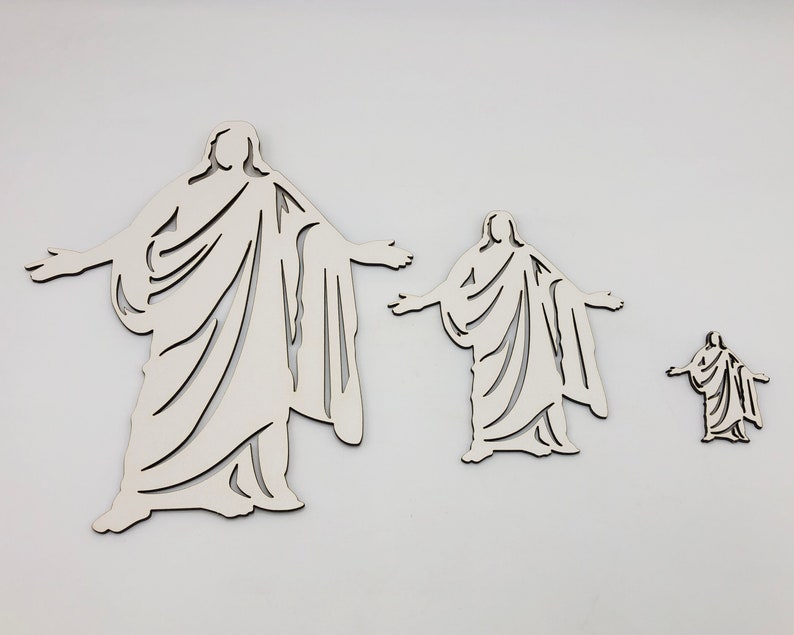 May include: Three white wooden cutout figures of a person in a robe with arms outstretched. The figures are different sizes.