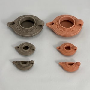 Puede incluir: Cinco l&aacute;mparas de aceite de terracota de diferentes tama&ntilde;os. Las l&aacute;mparas son todas marrones y tienen un dise&ntilde;o sencillo con un peque&ntilde;o agujero en el centro para la mecha. Las l&aacute;mparas est&aacute;n dispuestas en una fila de la m&aacute;s grande a la m&aacute;s peque&ntilde;a.